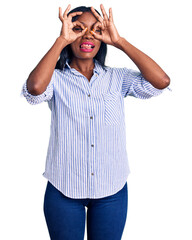 Fototapeta premium Young african american woman wearing casual clothes doing ok gesture like binoculars sticking tongue out, eyes looking through fingers. crazy expression.