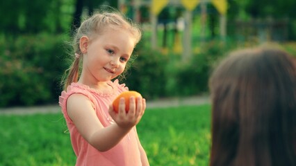 Happy family with orange in summer garden. Child girl gives orange fruit Mom in hands. Ripe oranges in hands kid. Useful vitamins from orchard. Healthy people, child. Concept healthy nutrition people
