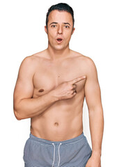 Fototapeta premium Handsome young man wearing swimwear shirtless surprised pointing with finger to the side, open mouth amazed expression.