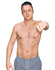 Fototapeta premium Handsome young man wearing swimwear shirtless looking unhappy and angry showing rejection and negative with thumbs down gesture. bad expression.