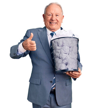 Senior handsome grey-haired man holding paper bin with crumpled document smiling happy and positive, thumb up doing excellent and approval sign