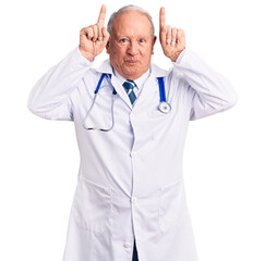 Senior handsome grey-haired man wearing doctor coat and stethoscope doing funny gesture with finger over head as bull horns