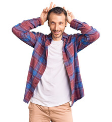 Young handsome man wearing casual clothes posing funny and crazy with fingers on head as bunny ears, smiling cheerful