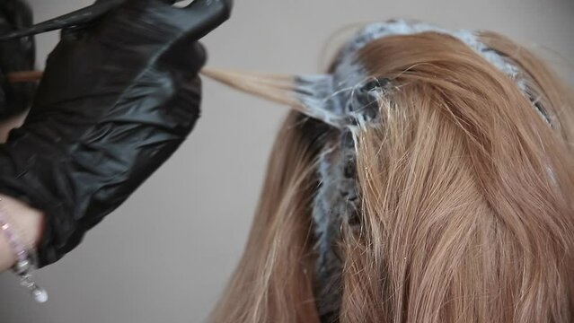 the master of hair coloring applies paint with brush to the head of red-haired woman, close-up