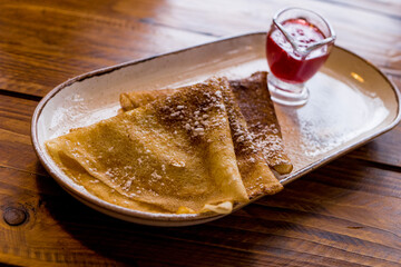 Pancakes with berry jam sprinkled with sugar on a plate on a wooden table