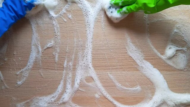 Cleaning process in kitchen. Deep Clean house in One Day concept. Two janitors in rubber gloves wash table with kitchen sponges and foam. Hands in motion close up. House cleaning services.