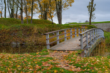 A wooden bridge in Kuressaare Park, located near the Kuressaare castle on a cloudy autumn day. Golden leaves on the ground. Kuressaare, Estonia.