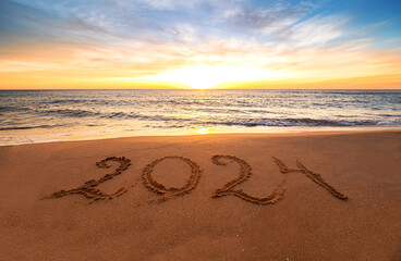 Happy New Year 2024 ocean sunrise on the beach. Written text on the sea beach at sunrise.