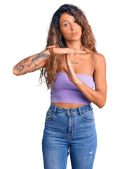 Young hispanic woman with tattoo wearing casual clothes doing time out gesture with hands,...