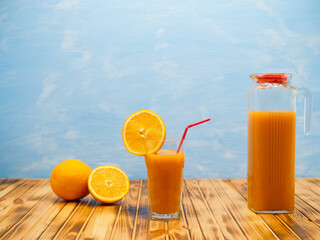 Natural orange juice in a jug on a wooden table on a blue background.