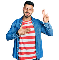 Young hispanic man with beard wearing casual denim jacket smiling swearing with hand on chest and...