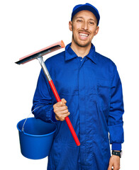 Bald man with beard wearing glass cleaner uniform and squeegee looking positive and happy standing...