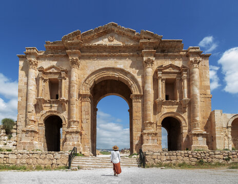 A mid-aged woman with her back turned standing in front of Hadrian's Arch in the archaeological city of Jerash