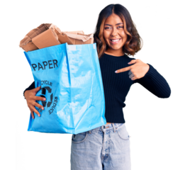Young beautiful mixed race woman holding recycling wastebasket with paper and cardboard smiling happy pointing with hand and finger