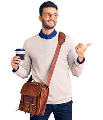 Young handsome hispanic man wearing leather bag and drinking take away coffee pointing thumb up to the side smiling happy with open mouth