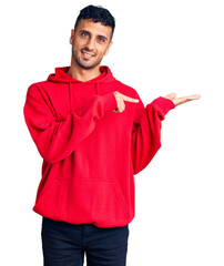 Young hispanic man wearing casual clothes amazed and smiling to the camera while presenting with hand and pointing with finger.