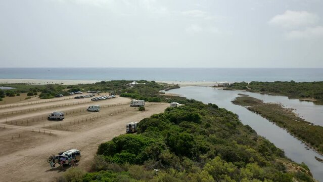 Aerial drone view of camper vans parked in wild Spiaggia di Berchida beach parking in Sardinia, Italy
