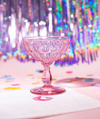 A Pink Champagne Vintage Coupe Glass with a Iridescent Tinsel background Party Scene - obrazy, fototapety, plakaty