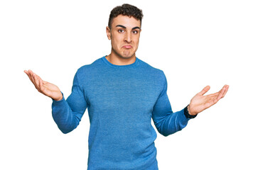 Hispanic young man wearing casual clothes clueless and confused expression with arms and hands...