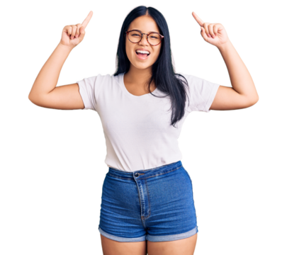 Young beautiful asian girl wearing casual clothes and glasses smiling amazed and surprised and pointing up with fingers and raised arms.