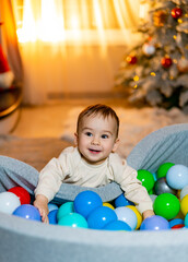 A Joyful Baby Surrounded by Colorful Balls and a Festive Christmas Tree. A baby in a ball pit with a christmas tree in the background