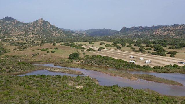 Aerial drone view of camper vans parked in wild Spiaggia di Berchida beach parking with mountain landscape in Sardinia, Italy