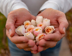Hands holding a delicate bouquet of peachy roses.