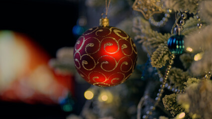 Christmas ball on Christmas tree. Cosy fireplace light in background. December winter mood. Background for holiday ads and offer.