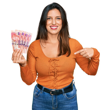 Beautiful hispanic woman holding south african 50 rand banknotes pointing finger to one self smiling happy and proud