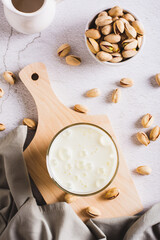 Alternative vegetarian pistachio milk in a glass and nuts on the table top and vertical view