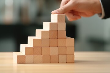 A person is seen placing a block into a pyramid structure. This image can be used to illustrate teamwork, problem-solving, construction, or building concepts