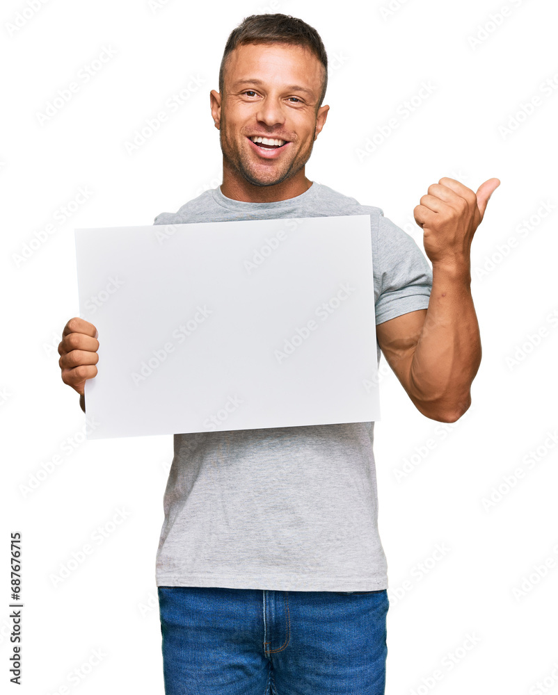 Sticker handsome muscle man holding blank empty banner pointing thumb up to the side smiling happy with open