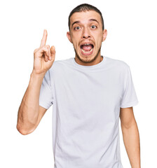 Fototapeta premium Hispanic young man wearing casual white t shirt pointing finger up with successful idea. exited and happy. number one.