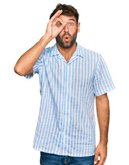 Fototapeta premium Handsome young man with beard wearing casual fresh shirt doing ok gesture shocked with surprised face, eye looking through fingers. unbelieving expression.