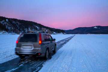 Winter travel. The car drives along an icy road along a frozen river bed against the backdrop of...