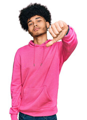 Young african american man with afro hair wearing casual pink sweatshirt looking unhappy and angry showing rejection and negative with thumbs down gesture. bad expression.