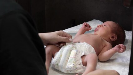 Mother changing diaper on her newborn baby indoors. Little legs of a newborn baby. The child moves his legs. New life. Dry skin of the baby