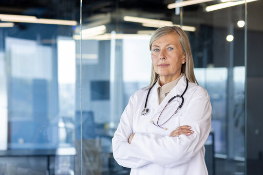 Portrait of a scary gray-faced Inca doctor standing in a white coat in a hospital office with his arms crossed and looking seriously at the camera.