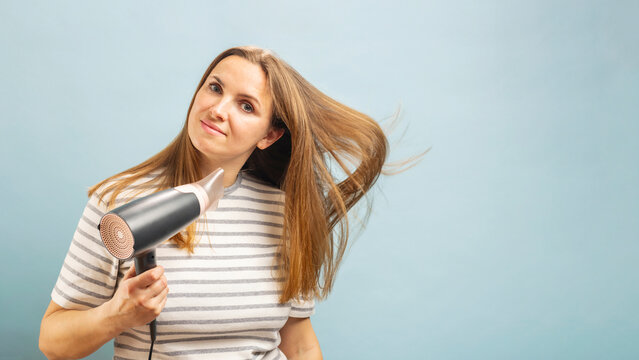 Beautiful young woman using hair dryer on light blue background