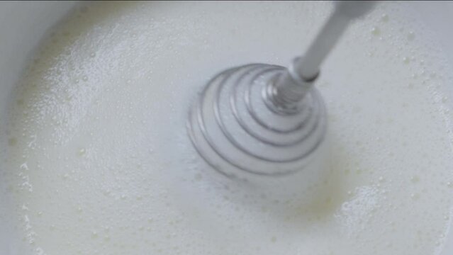 Whipping cream using hand whisk, close-up.