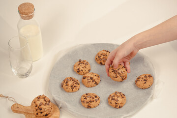 Hands take fresh cookies from plate, close-up,Close-up of hand grabbing a freshly baked cookie on white background with milk bottle and glass