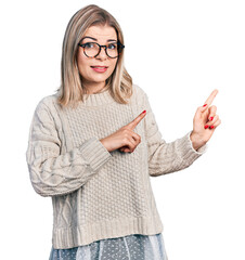 Young blonde woman wearing glasses pointing aside worried and nervous with both hands, concerned and surprised expression