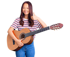 Fototapeta premium Young beautiful chinese girl playing classical guitar smiling happy and positive, thumb up doing excellent and approval sign