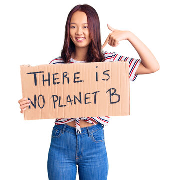 Young beautiful chinese girl holding there is no planet b banner pointing finger to one self smiling happy and proud