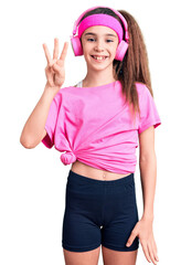 Fototapeta na wymiar Cute hispanic child girl wearing gym clothes and using headphones showing and pointing up with fingers number three while smiling confident and happy.