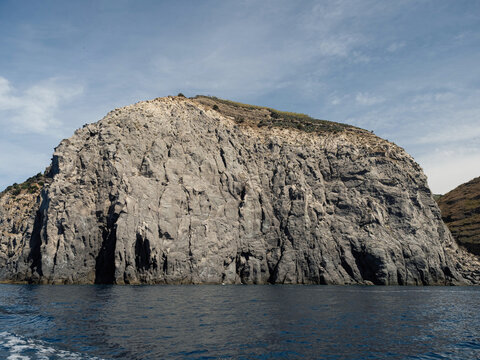 Weathered seaside rock face texture with parts of green and blue water. Aged volcanic stone wall surface background pattern with cracks and scratches. Banner. Ischia Island, Italy.