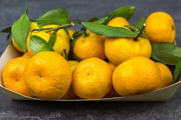 orange tangerines with green leaves in a cardboard tray on a table