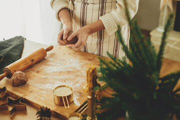 Hands kneading gingerbread dough with rolling pin, cooking spices, festive decorations on rustic...