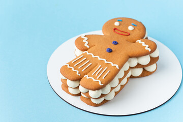 Traditional Christmas honey gingerbread man cake with buttercream filling sprinkled with powdered sugar like a snow flakes on the blue pastel background. Merry Christmas and happy New Year concept.