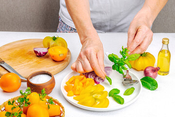A woman is preparing a tomato salad. Ripe vegetables, herbs, aromatic spices, olive oil